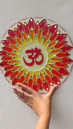 a person's hand holding up a colorful plate with an om shan symbol on it