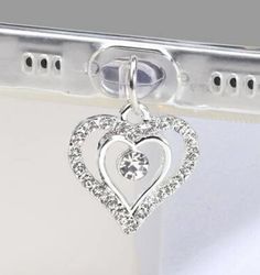 a heart shaped diamond pendant hangs from a metal hook on a white background with the word love written below it