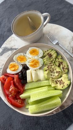 a white plate topped with cucumbers, tomatoes and hard boiled eggs next to a cup of tea