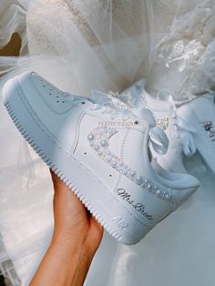 a person holding up a white sneaker with pearls on the side and an embellished bow at the top