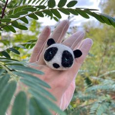 a small stuffed panda bear sitting on top of a palm tree branch in someone's hand