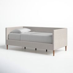 a gray couch with white pillows on it and two wooden legs, sitting in front of a white wall