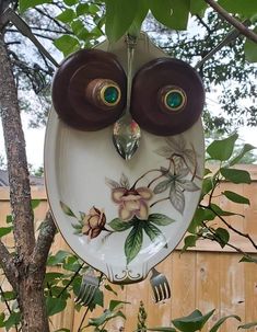 an owl shaped plate hanging from a tree with leaves and flowers painted on it's face