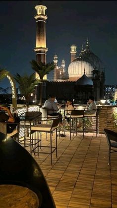 people are sitting at tables on the roof of a building with an illuminated tower in the background