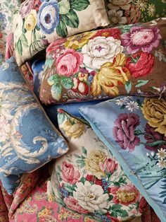 a pile of pillows sitting on top of a bed covered in floral print covers and pillow cases