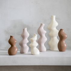 five ceramic vases lined up in a row on a shelf against a white wall