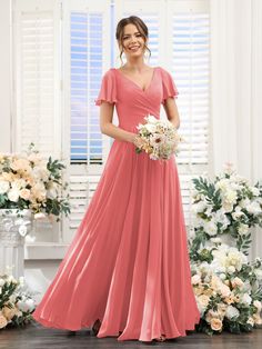 a woman in a long pink dress standing next to white flowers and holding a bouquet