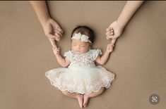 a baby is being held by two hands while wearing a white dress and holding her mother's hand