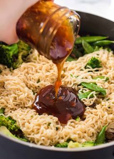 someone pouring sauce over noodles and broccoli in a skillet