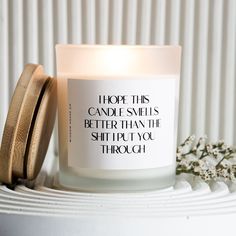 a candle with a quote on it sitting next to some flowers and a flower pot