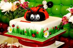 a ladybug cake sitting on top of a table with flowers and balloons in the background