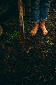 a person standing in the dirt with their bare feet propped up against a fence post