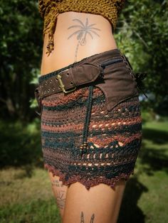 a woman with tattoos on her stomach wearing a skirt and belted shorts is standing in the grass