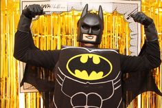 a man dressed as batman standing in front of a gold curtain with his hands up