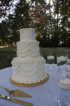 a white wedding cake sitting on top of a table next to silverware and candles