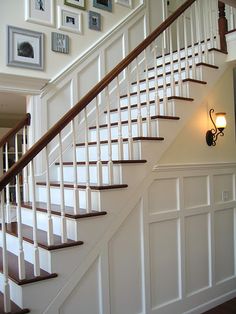 there is a white stair case in the house with pictures on the wall behind it