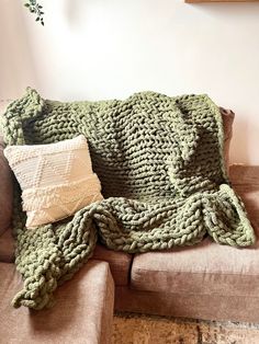 a green knitted blanket sitting on top of a brown couch next to two pillows