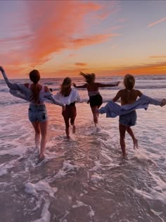 four girls are running into the ocean at sunset