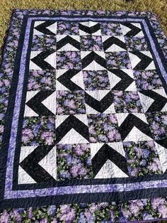 a black and white quilt with purple flowers in the center, on top of grass