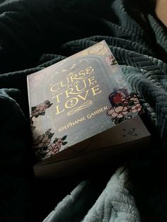 the book curse of true love is laying on top of a blue blanket with flowers