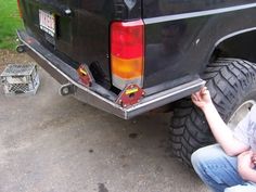 a woman sitting on the ground next to a truck with its tire in front of her