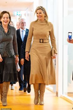 two women walking down a hallway with other people behind them and one woman holding a cell phone in her hand