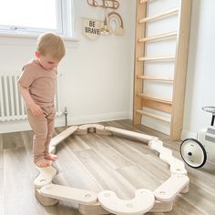 a young boy standing on top of a wooden play structure in the middle of a room