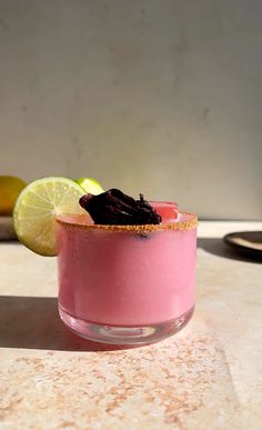 a pink drink garnished with black stuff and limes on a counter top