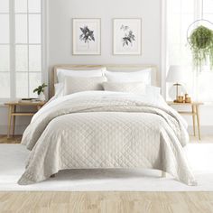 a bed with white sheets and pillows in a room next to two pictures on the wall