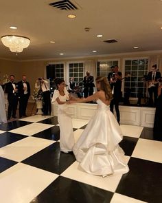 two women in white dresses dancing on a black and white checkered dance floor with other people