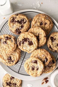 chocolate chip cookies on a cooling rack next to a cup of milk and a glass of milk