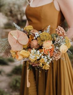 a woman holding a bouquet of flowers in her hands and wearing a brown dress with yellow accents