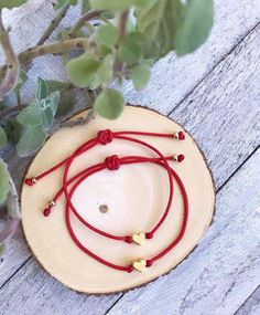 three red string bracelets with gold hearts on them sitting next to a potted plant