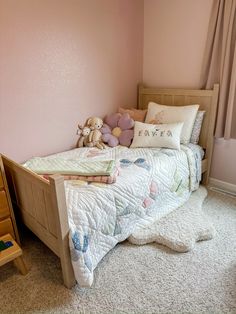 a small child's bedroom with pink walls and white carpeted flooring, teddy bear on the bed