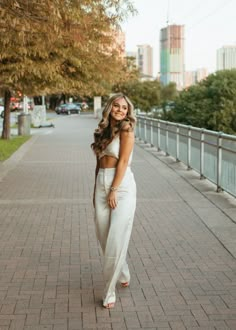 a woman standing on the sidewalk wearing a white dress