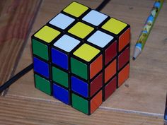 a rubik cube sitting on top of a wooden table next to a pen and pencil