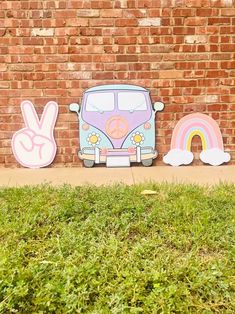 three wooden cutouts of vw camper van, peace sign and rainbow on the side of a brick wall