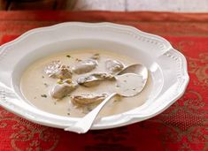 a white bowl filled with soup sitting on top of a red table cloth next to a silver spoon