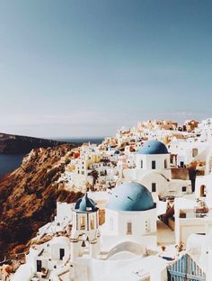 an aerial view of white buildings and blue domes on the cliff side, with a body of water in the background