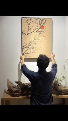 a man holding up a piece of art in front of a painting on the wall