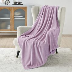 a chair with a pink blanket on it in front of a white rug and wooden cabinet