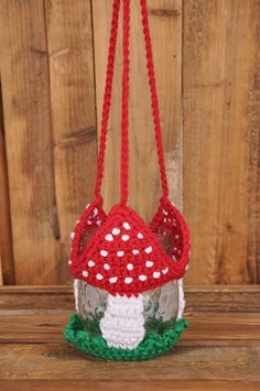 a crocheted red and white mushroom hanging from a string on a wooden surface