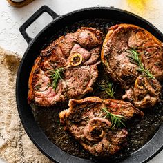 steaks in a cast iron skillet with rosemary garnish on the side