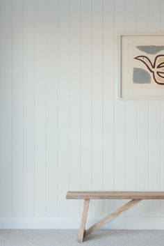 a wooden bench sitting in front of a wall with a painting hanging on it's side