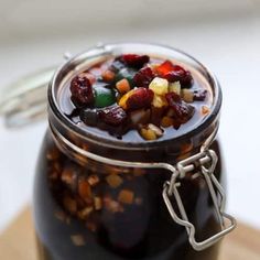 a jar filled with fruit and nuts sitting on top of a wooden table next to a spoon