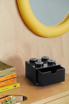 there is a black lego block on the desk next to some books and a mirror