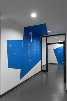 an empty hallway with white walls and blue graphic on the wall, leading to another room