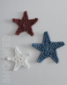 three crocheted stars are shown on a white surface, one is red and the other is blue