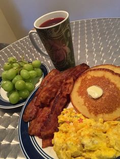 a breakfast plate with eggs, bacon, pancakes and grapes next to a cup of coffee