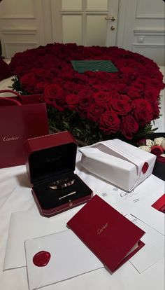 red roses are arranged around the ring box and other items on top of a table